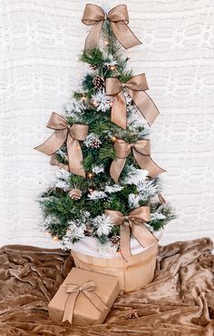 a small christmas tree with brown bows and pine cones in a gift box on a bed