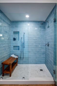 a walk in shower sitting next to a wooden bench under a sky blue tiled wall