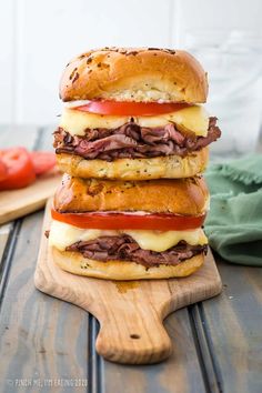 a stack of sandwiches sitting on top of a wooden cutting board next to tomatoes and cheese