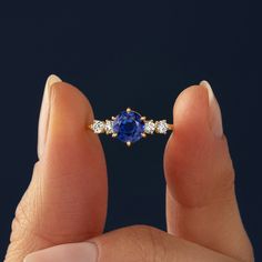 a woman's hand holding an engagement ring with a blue sapphire and three diamonds