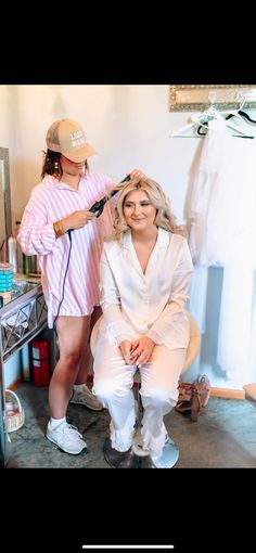 a woman is getting her hair styled by a man in a pink shirt and white pants