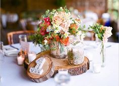 there are many vases with flowers in them sitting on the wooden slab at the table