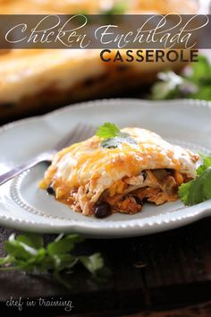 an enchilada on a white plate with a fork and green garnish