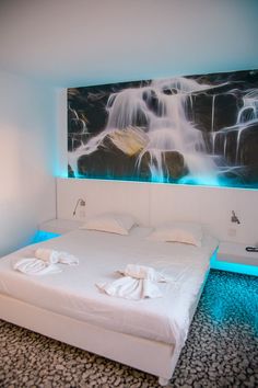 a bed with white sheets and towels on it in front of a waterfall wall mural