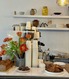 there are many plates and cups on the counter with flowers in them, along with bread