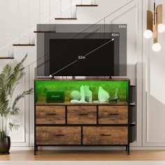 a television on top of a wooden dresser next to a stair case and potted plant