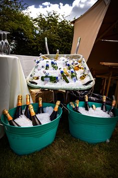 several buckets filled with bottles and ice on top of a grass covered field next to a tent