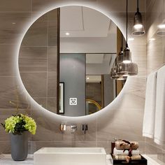 a bathroom sink under a round mirror with lights on the wall and flowers in a vase