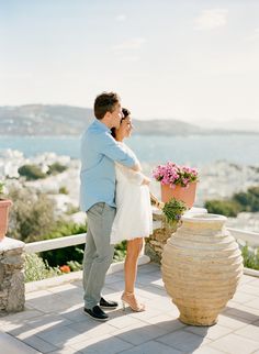 a man and woman standing next to each other on top of a building near the ocean