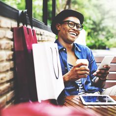 a man sitting on a bench holding a cup and looking at his cell phone while smiling