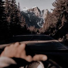 someone is driving down the road with their hand on the steering wheel and mountains in the background