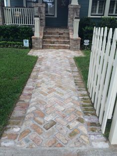 a brick walkway leading to a house with a white picket fence