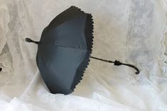 an open umbrella laying on top of a white lace covered tablecloth with black handles