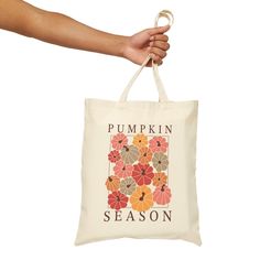 a person holding a bag with the words pumpkin season printed on it and an orange flower design