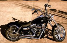 a black motorcycle parked on top of a cement floor next to a wall and tree