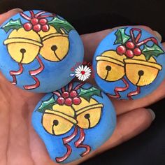 three painted rocks in the shape of bells with bows and holly berries on each rock