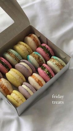 a box filled with different colored macaroons on top of a white cloth covered table