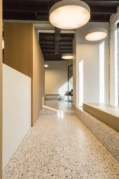 an empty hallway with two round lights hanging from the ceiling and windows on either side