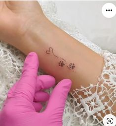 a person with gloves on their hands is holding a small tattoo that has hearts and paw prints