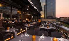 an outdoor dining area with tables, chairs and candles lit up at night in front of the city skyline