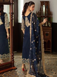 Embroidered Pakistani Suit In Navy Blue Color is a bold ensemble with some magnificent gold embellishments crafted on it giving it a royal yet charming look. This Pakistani Party Dress can be stitched in two styles according to the demand of our lovely customers. Gown: This Embroidered Pakistani Suit comes with a beautiful gown in open style half-cut. The fabric of this gown is organza and is beautifully emblazoned with fine embroidery, tilla, and iridescent sequins. Heavily embellished neckline Festive Unstitched Suit With Gold Embroidery For Eid, Festive Gold Embroidery Unstitched Suit For Eid, Eid Festive Unstitched Suit With Gold Embroidery, Eid Chanderi Salwar Kameez With Gold Embroidery, Eid Chanderi Sets With Gold Embroidery, Festive Unstitched Suit With Gold Embroidery, Unstitched Suit With Gold Embroidery For Festive Occasions, Eid Sets In Raw Silk With Gold Embroidery, Bollywood Style Unstitched Suit With Gold Embroidery For Eid