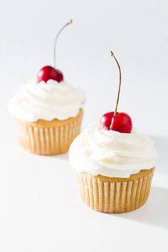 two cupcakes topped with whipped cream and cherries