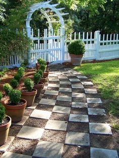 several potted plants in front of a white picket fence and garden path with cobblestone pavers