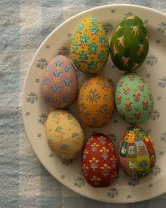 six painted eggs in a white bowl on a tablecloth with blue and yellow flowers