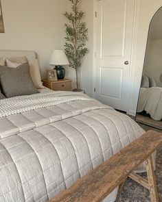 a bedroom with a bed, mirror and wooden bench in front of the door that leads to another room