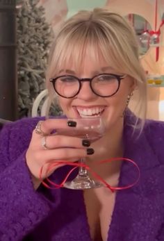 a woman wearing glasses holding a wine glass in front of her face and smiling at the camera