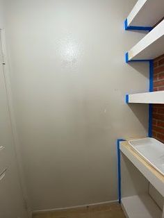 an empty room with shelves and blue tape on the wall, in front of a brick wall