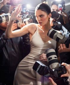 a woman in a white dress is surrounded by photographers