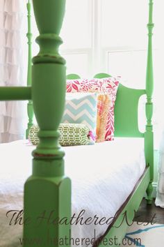 a green bed frame with white sheets and pillows on it in front of a window