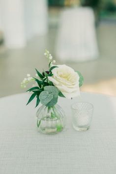 two vases with white flowers and greenery on a table