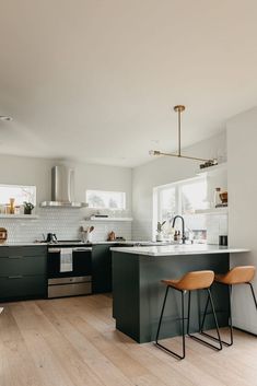 two stools are in the middle of a kitchen with black cabinets and white countertops