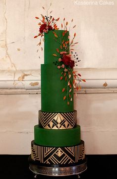 a three tiered green cake with red flowers on top and gold trimmings