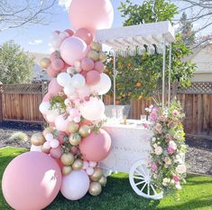 a table topped with balloons and flowers on top of green grass next to a white cart