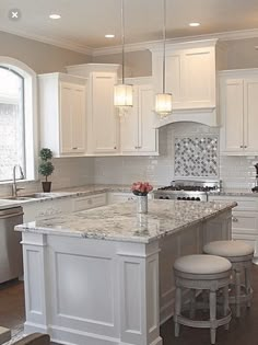 a large kitchen with white cabinets and marble counter tops, along with two stools