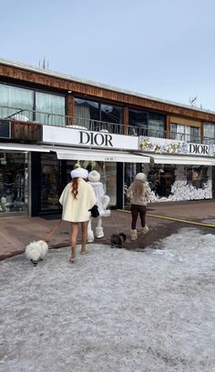 two people are walking their dogs in front of a dior store with snow on the ground