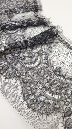 two pieces of black lace with beads and sequins on white tablecloth, close up