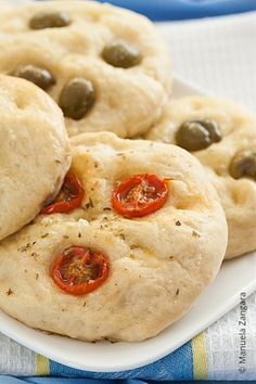 three cookies with tomatoes and olives on a white plate next to a blue towel