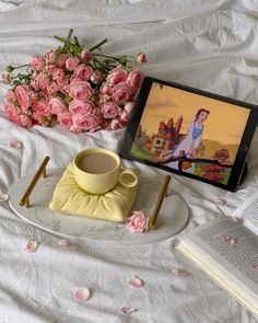 a tablet computer sitting on top of a table next to pink flowers and a cup