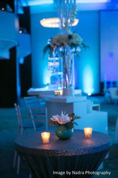 a table with candles and flowers on it in front of a blue lit up room