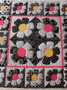 a black and white quilt with pink, yellow, and gray flowers on the center