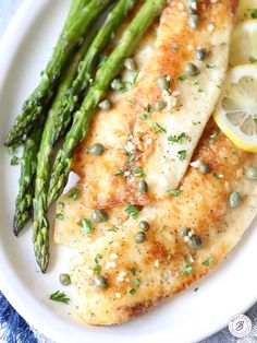 a white plate topped with chicken, asparagus and lemon slices on top of it