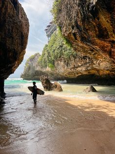 a person holding a surfboard walking into the water near some large rocks and cliffs