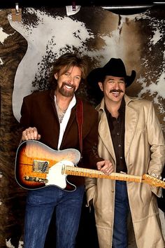 two men standing next to each other holding guitars