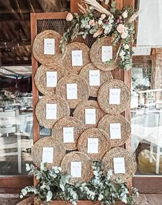 a table with place cards and flowers on it in front of a wooden frame filled with wicker plates