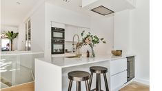 a white kitchen with two stools next to the counter top and an oven in the background