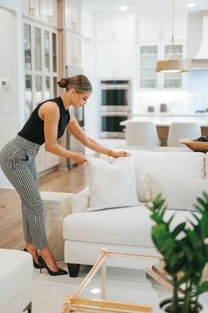 a woman placing pillows on a couch in a living room